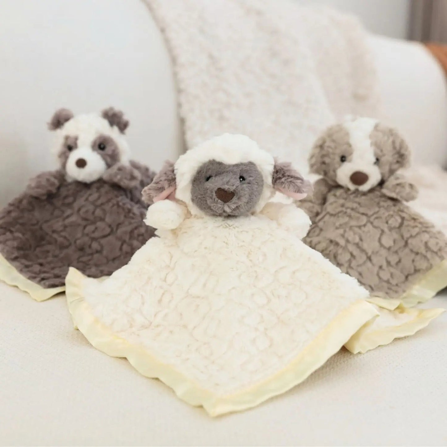 Three plush toys resembling a sheep, bear, and badger on a white blanket.