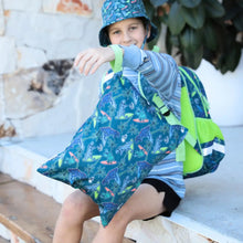 Load image into Gallery viewer, Child wearing a blue jacket with dinosaur pattern and green backpack sitting outdoors.