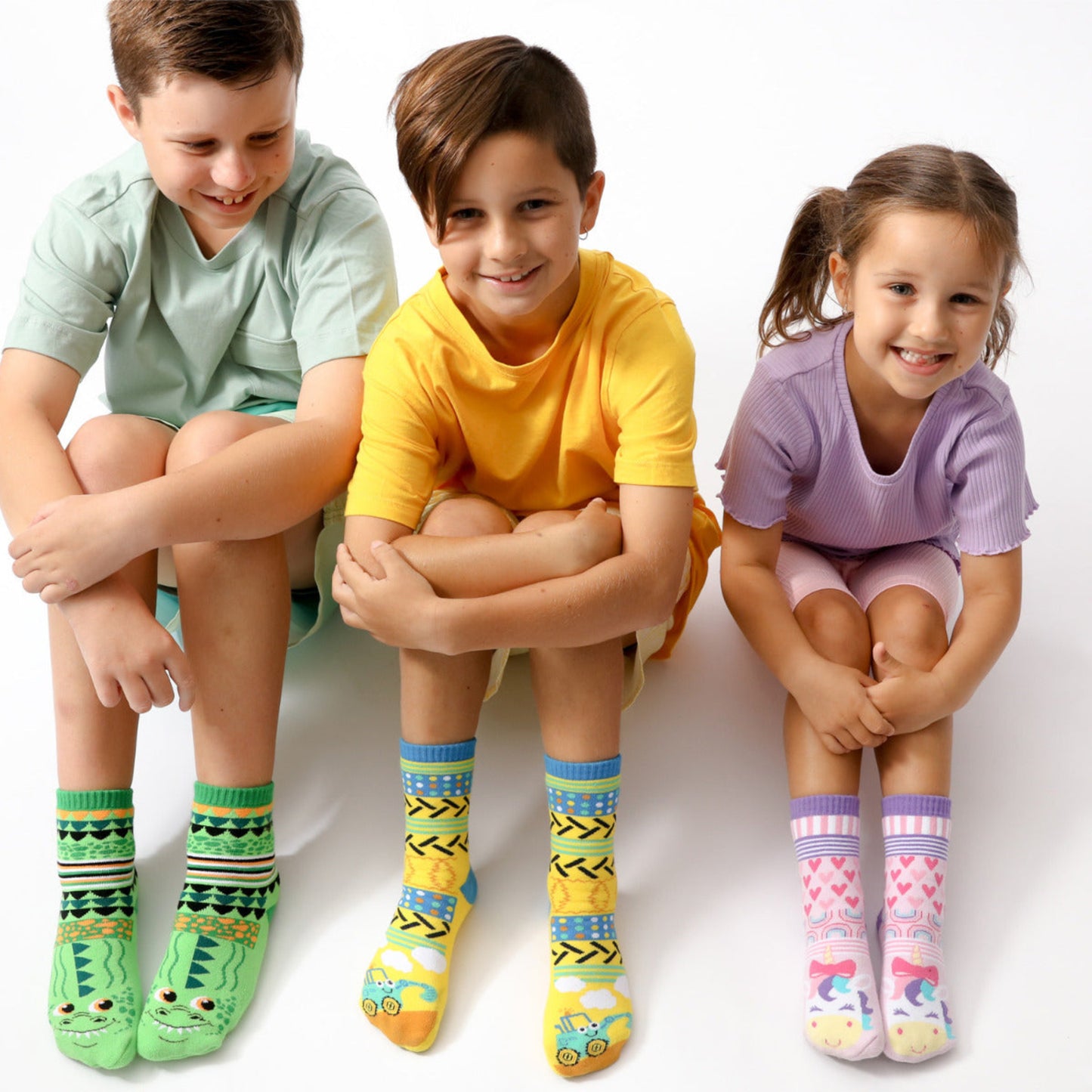 Three children sitting side by side wearing colorful socks on a white background