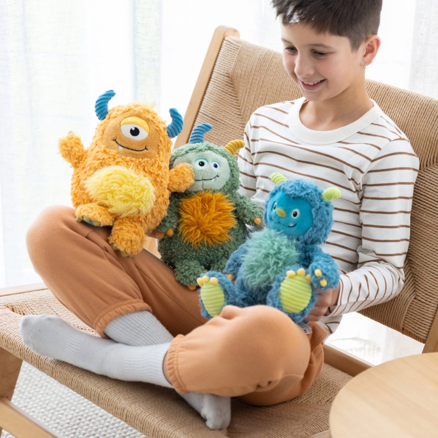 Child sitting on a couch holding three colorful plush monsters.