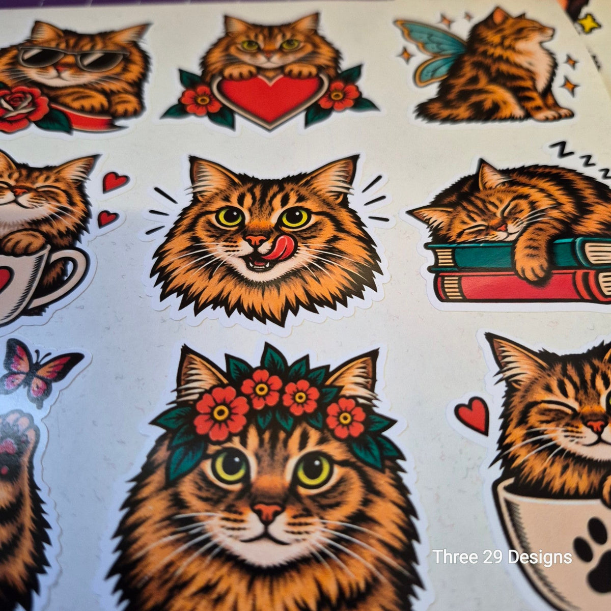 A sheet of die-cut cartoon cat stickers with traditional tattoo-style illustrations. The cats include sunglasses, a heart, a fairy, books, a cup, a flower crown, and sleeping poses, all on a white background.