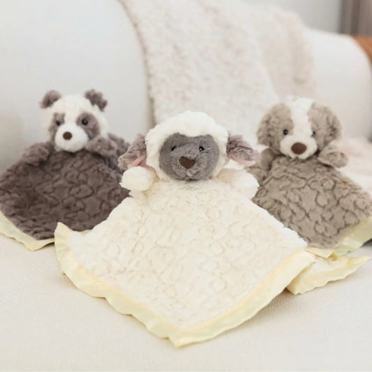 Three plush toys resembling a sheep, bear, and badger on a white blanket.