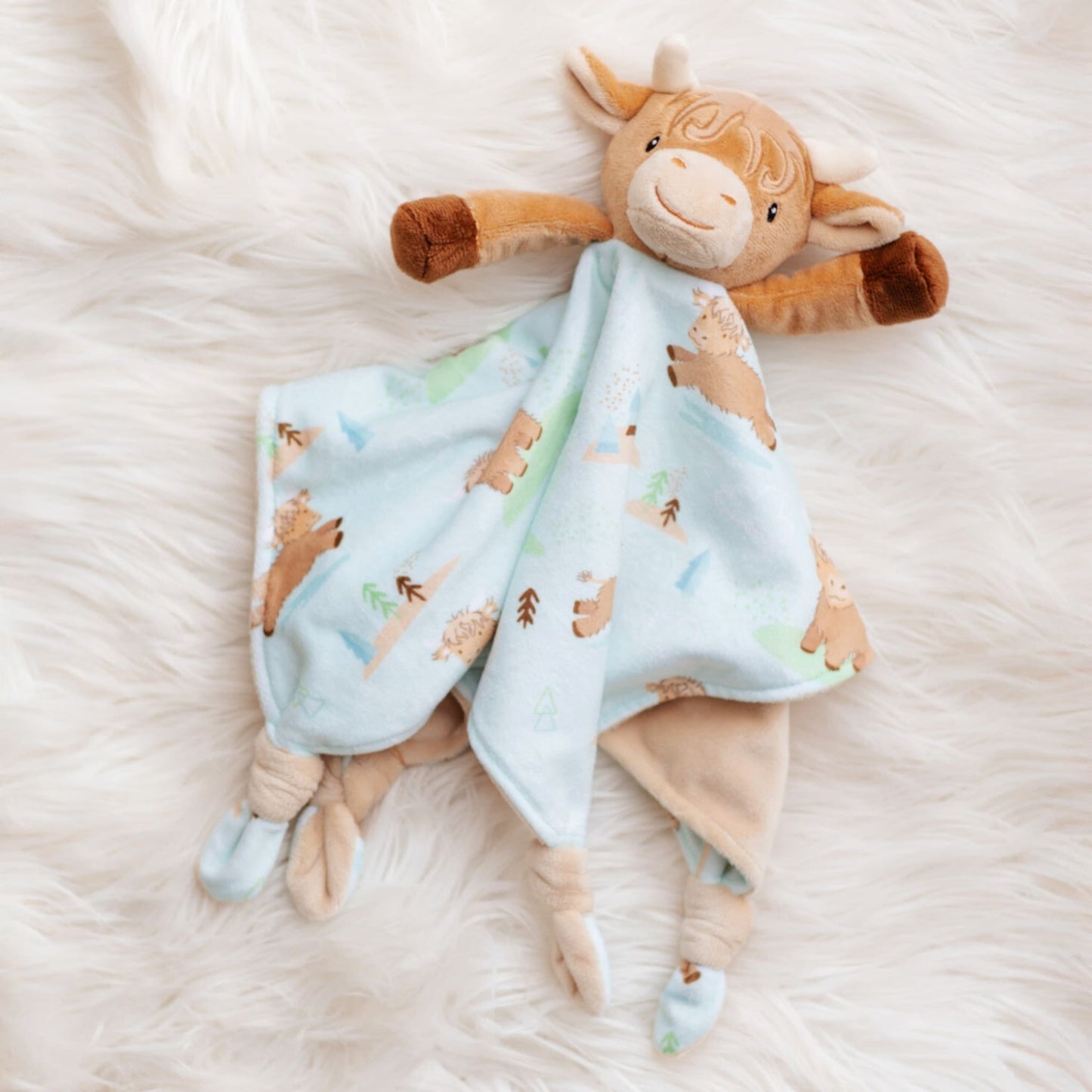 Plush toy cow with a matching blanket on a soft white surface