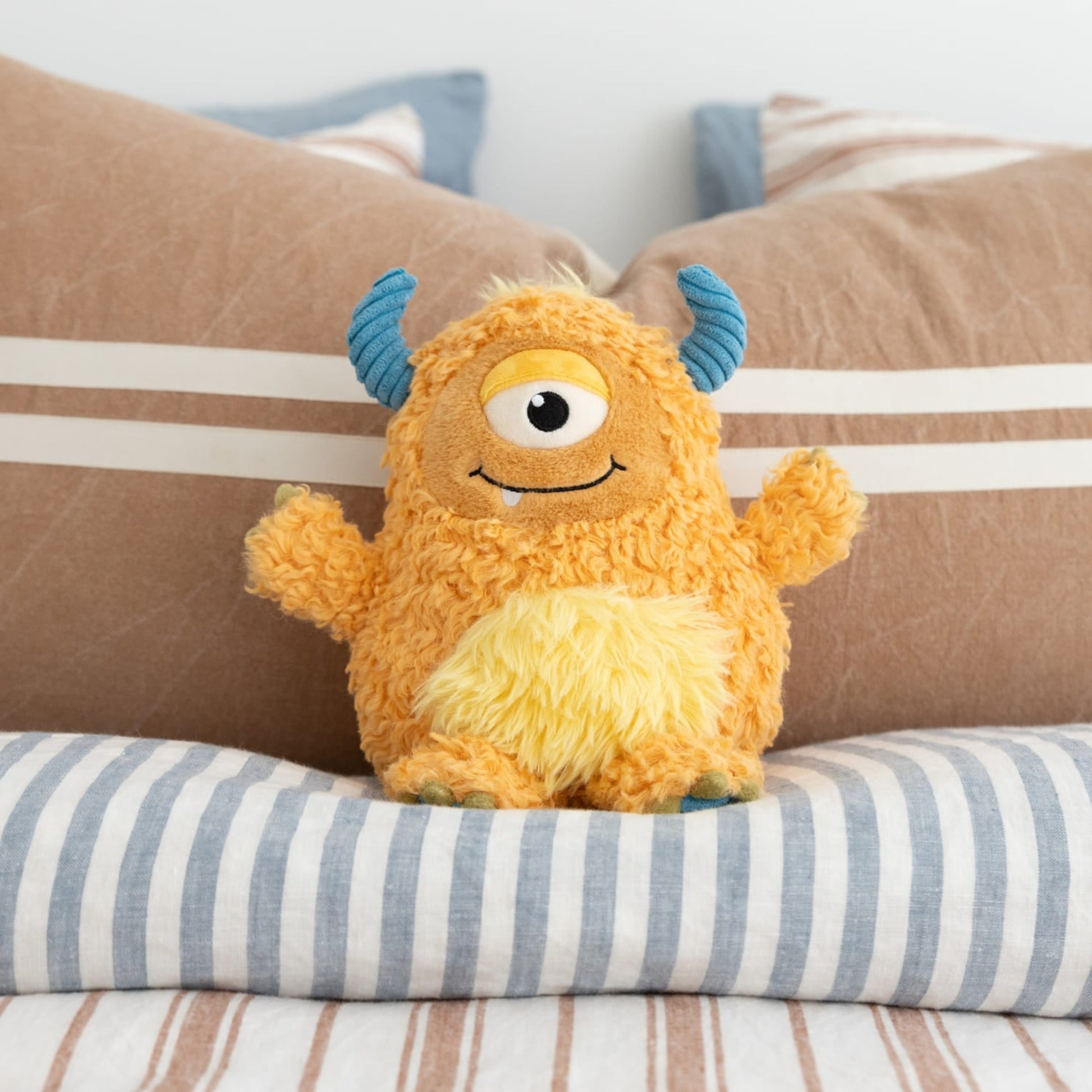 Plush toy monster with blue horns on a striped pillow