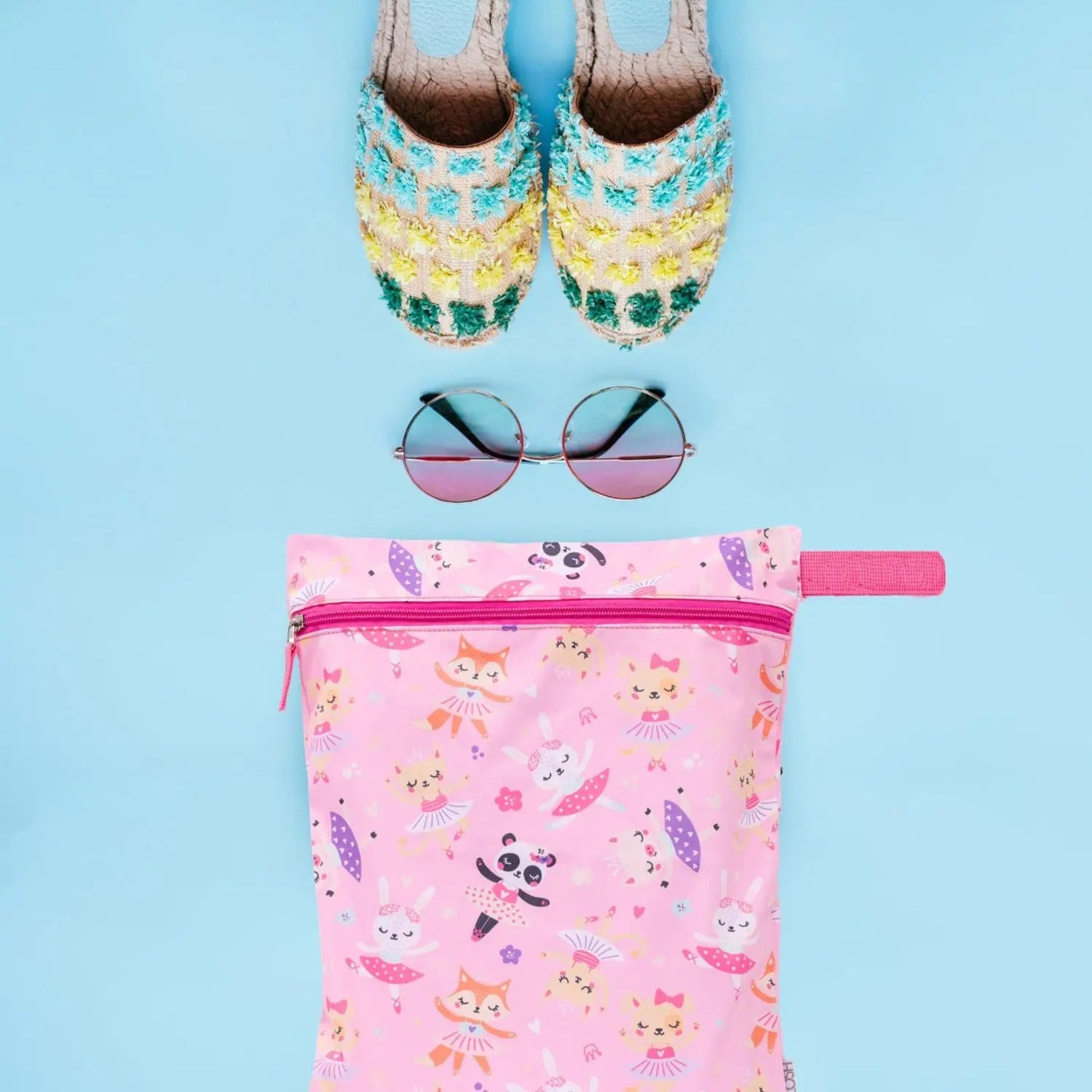 Colorful slippers, sunglasses, and a pink pouch with animal prints on a blue background