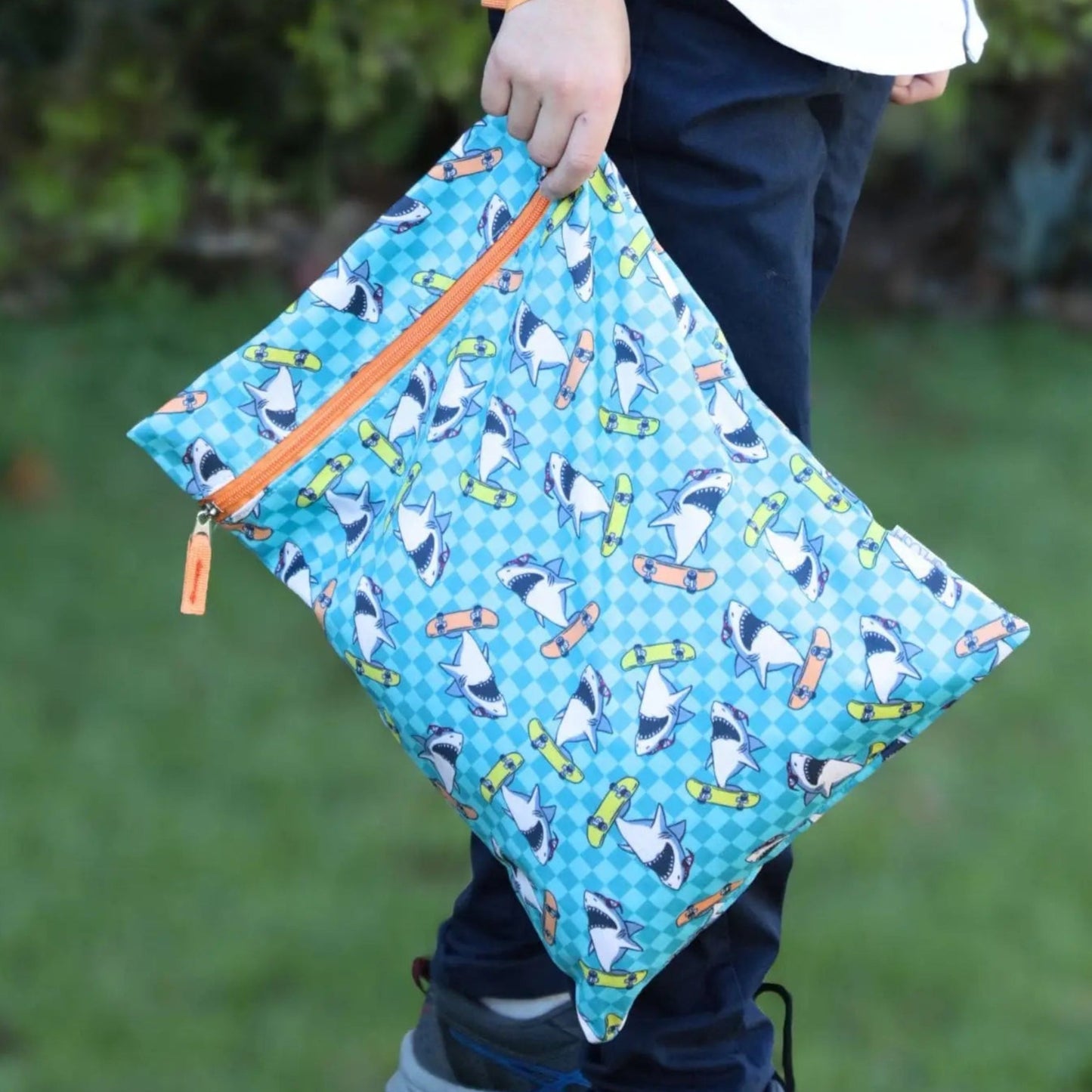 Person holding a blue patterned pouch with orange zipper outdoors
